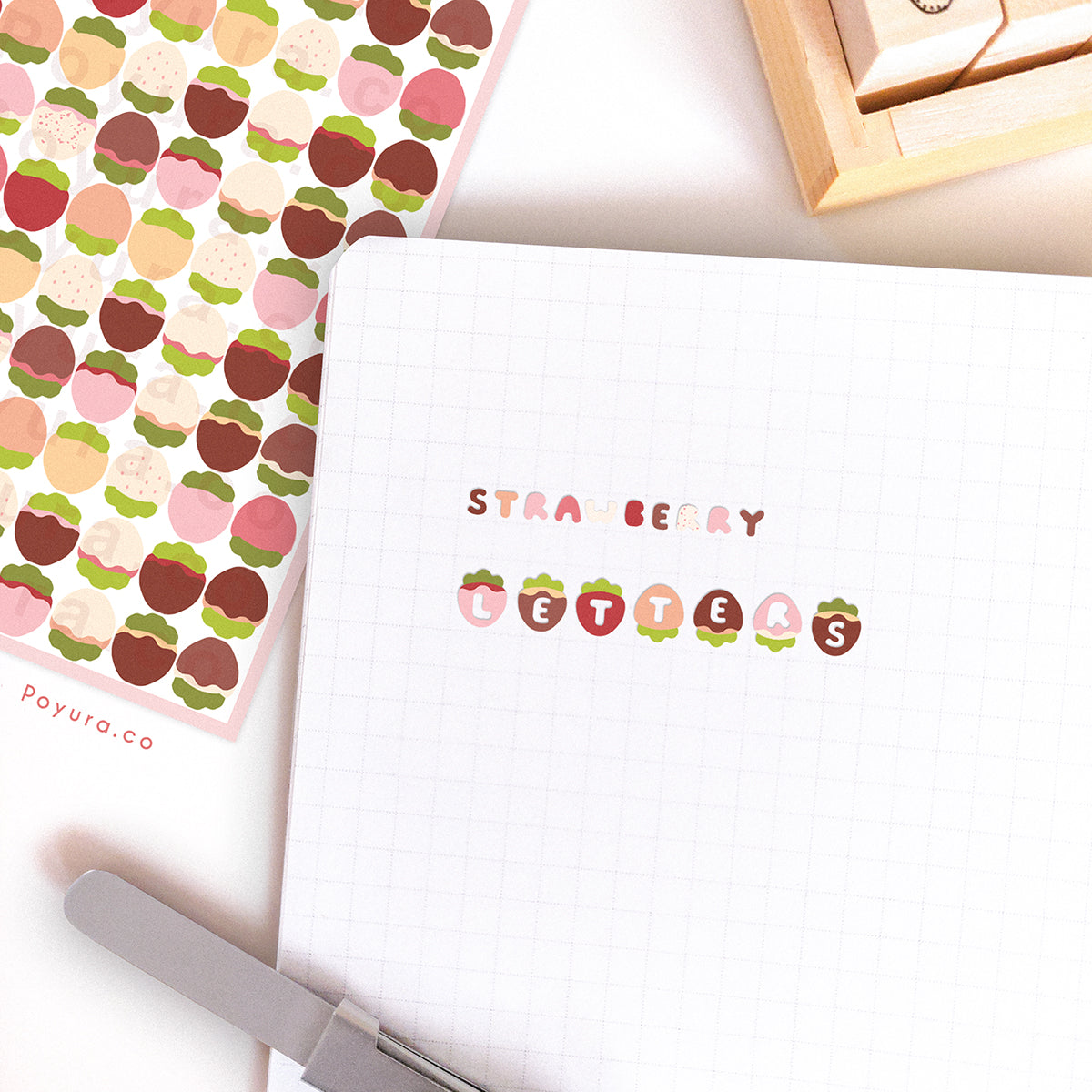 A journal spread that has strawberry stickers pasted on it. The strawberries have a letter cutout in the center.