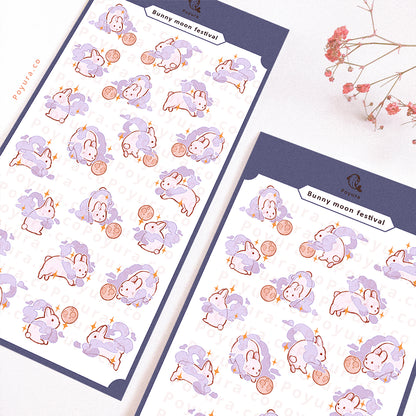 Sticker sheet of white bunnies with a purple cloud around them. They are playing with a moon as a ball.