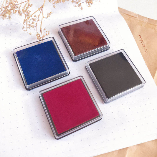 4 ink pads placed on top of an open notebook. The ink pads are in the colors blue, brown, red, and black. 