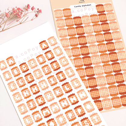 Two sticker sheets of orange candies with alphabet letter cutouts in the center.