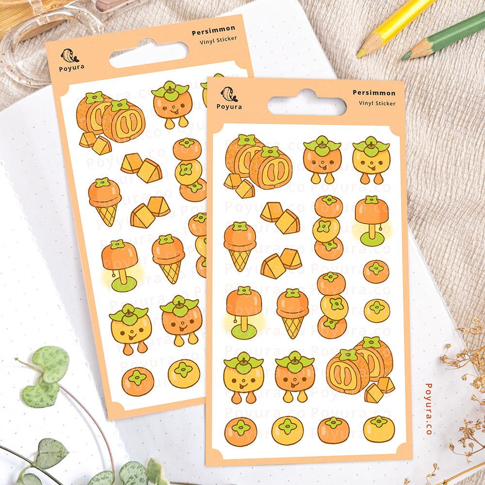 Persimmon sticker sheet on an open notebook. The desk is decorated with pencils, a scissor, and some plants.