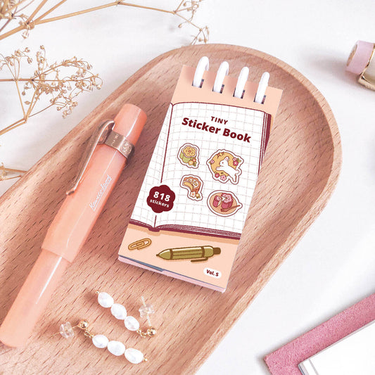 Pink pen and sticker book on a wooden tray with decorative elements